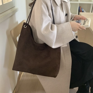 Detail of a large brown suede tote bag with slim shoulder straps and metal side eyelets