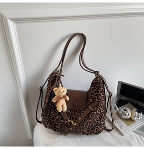 Close-up of leopard print hobo bag with brown leather straps and a plush bear charm