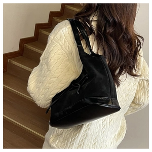 Detail of black contrast texture bucket bag with bow drawstring on a beige sweater