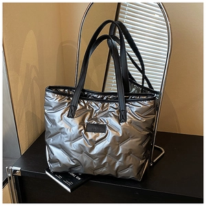 Close-up of quilted metallic silver tote bag with leather straps and logo patch