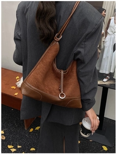 Brown suede hobo bag with silver ring detail worn by a model in an autumn street setting