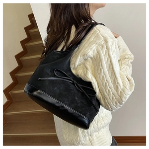 Detailed side view of a black retro bucket bag with a bow on a textured knit sweater
