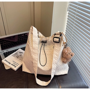 White textured drawstring bucket bag with plush bear charm in a cozy indoor setting