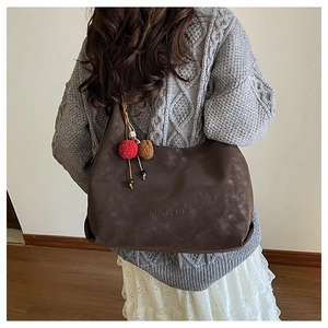 Détail d'un sac cabas marron foncé à texture mate et pompon décoratif bicolore