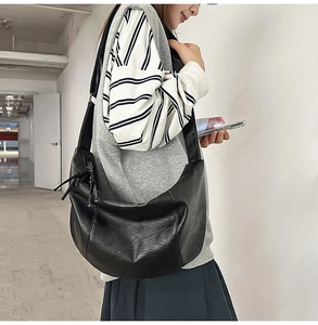 Détail d'un grand sac demi-lune noir en similicuir avec bandoulière large et texture lisse
