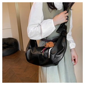 Detail shot of a black leather crescent hobo bag with a brown teddy bear pendant charm