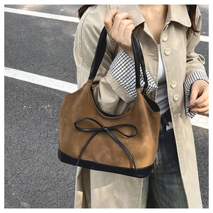 Brown and black bicolor bucket bag with bow detail worn by a model in a trench coat
