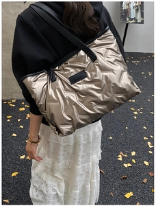 Quilted champagne tote bag shown on shoulder with black logo patch and metallic finish