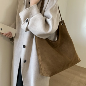 Brown suede tote bag with slim shoulder straps worn by model in minimalist indoor setting