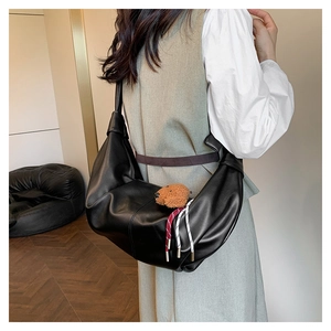 Detail view of black matte crescent shoulder bag with brown plush bear charm accessory