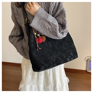 Détail du grand sac cabas noir avec pompon bicolore et logo gravé sur la surface mate