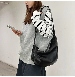 Sac hobo minimaliste en cuir noir à grain naturel porté par un mannequin pour le quotidien