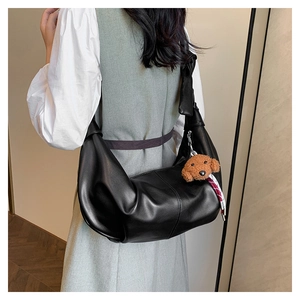 Detail of black faux leather croissant bag with cute dog pendant and striped ribbon