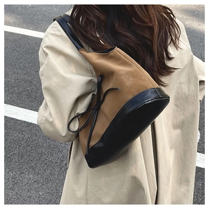 Detail of minimalist two-tone bucket bag with leather contrast and side bow accent