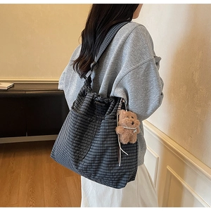 Detail of checkered bucket bag with drawstring closure and brown plush bear charm