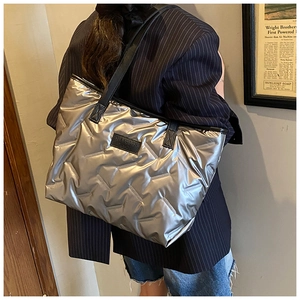 Detail of silver quilted tote bag featuring metallic finish and black logo strap