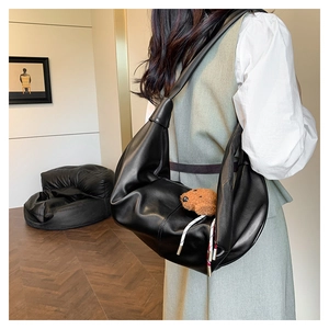 Detail view of black crescent shoulder bag with a cute brown plush bear charm