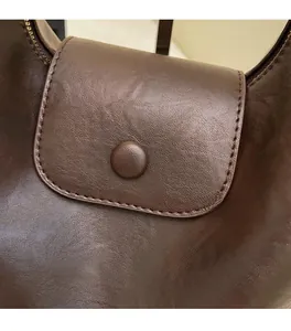 Close-up of retro brown faux leather shoulder bag with round snap button and curved flap