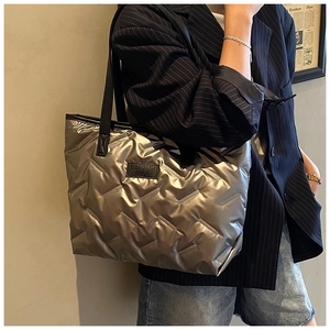 Detailed quilted texture of metallic tote bag with black shoulder strap and logo patch