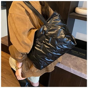 Detail of black glossy quilted tote bag with wide strap and brand label on side