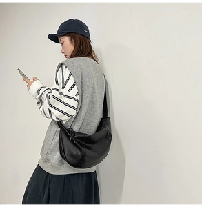 Détail d'un sac hobo en cuir noir avec nœud de serrage latéral sur un mannequin femme