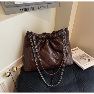 Détail du sac seau matelassé en cuir marron foncé avec bandoulière chaîne sur un tabouret