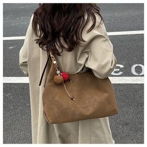 Détail du sac fourre-tout en daim marron avec pompon décoratif porté par un mannequin