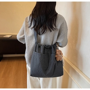 Detail view of dark plaid drawstring bucket bag with a cute plush bear pendant accessory