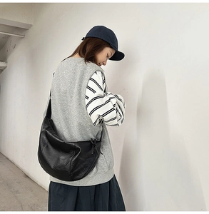 Détail d'un sac à bandoulière en demi-lune noir minimaliste en cuir PU souple sur modèle