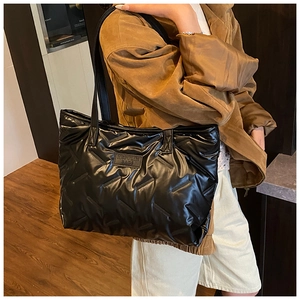 Detail of black quilted tote bag with glossy finish and brand logo on shoulder strap