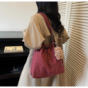 Detail of red checkered canvas tote bag featuring drawstring closure and plush bear charm