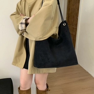Detail of a large matte black tote bag paired with a beige coat and brown boots