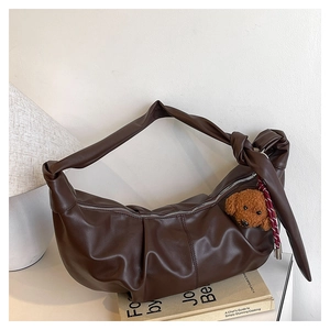 Close-up of brown pleated dumpling bag with soft leather texture and plush bear charm
