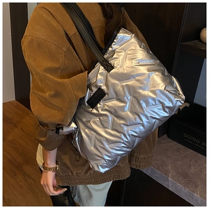 Detailed view of shiny silver quilted tote bag with black straps in a cozy indoor setting