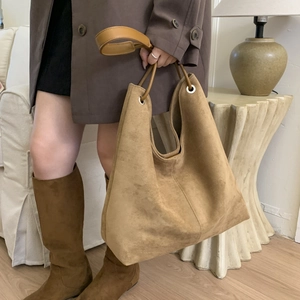 Detail of a large dark camel suede tote bag with metal eyelets and a single shoulder strap