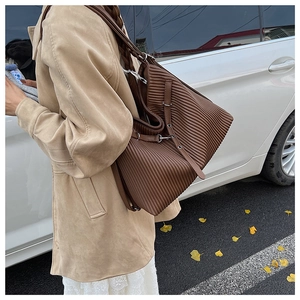 Detail of a large brown tote bag with vertical pleats and leather strap on a model