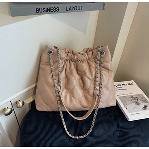 Détail macro du sac seau matelassé beige avec motifs floraux et bandoulière chaîne