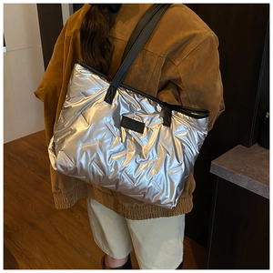 Silver quilted puffer tote bag shown on shoulder with reflective metallic texture