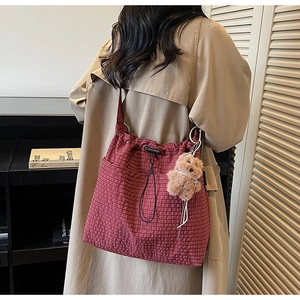 Detail of dark red checkered bucket bag with drawstring closure and plush bear charm