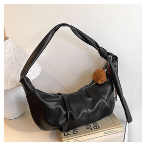 Detail of black faux leather hobo bag with knotted strap and teddy bear plush charm