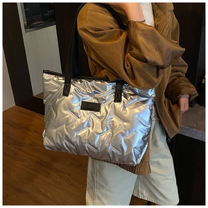 Detail showing shiny silver quilted tote bag with black strap and metallic texture