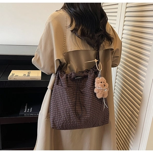 Brown checkered drawstring bucket bag with plush pendant on a model in trench coat