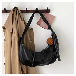 Macro detail of black pleated PU leather shoulder bag with decorative knotted strap and plush charm