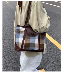 Detail of vintage plaid tote bag with brown leather trim shown on shoulder