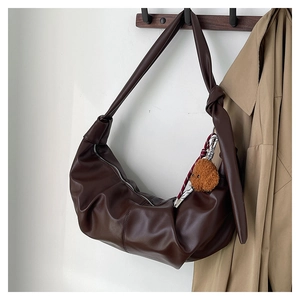 Detail of dark brown leather crescent bag featuring a knotted strap and plush bear charm