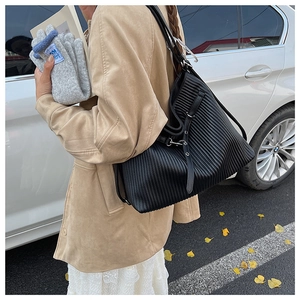 Close-up of black pleated leather tote bag showing vertical textures and silver metal buckles