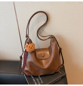 Close-up of brown PU leather shoulder bag with plush bear charm on a design book