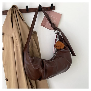 Detail of a brown leather crescent bag featuring a knotted strap and a teddy bear charm