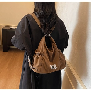 Dettaglio borsa in tela marrone scuro con pieghe, tracolla e stemma del logo brand