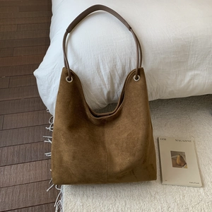 Detail view of large brown suede tote bag with leather strap in a cozy home setting